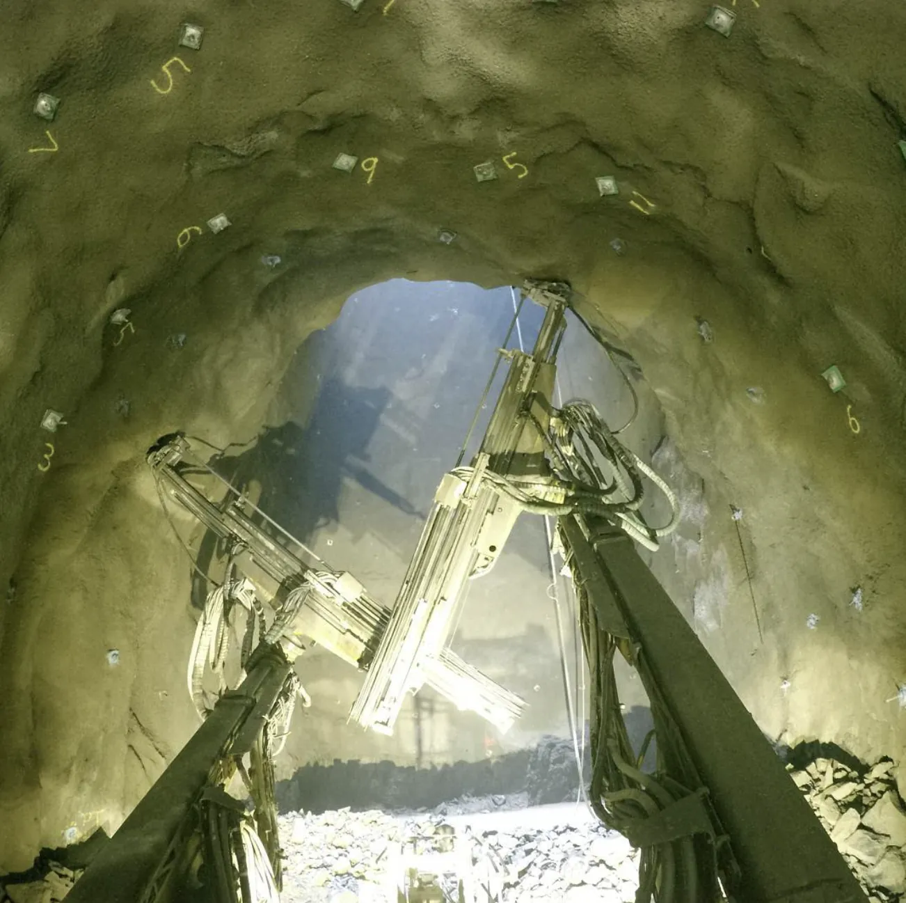 Looking up a shaft past two drill booms, with bolt plates numbered in paint.